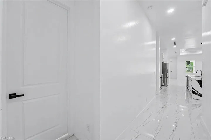 Hallway featuring white walls, recessed lighting, and large format white tile flooring with dark veining