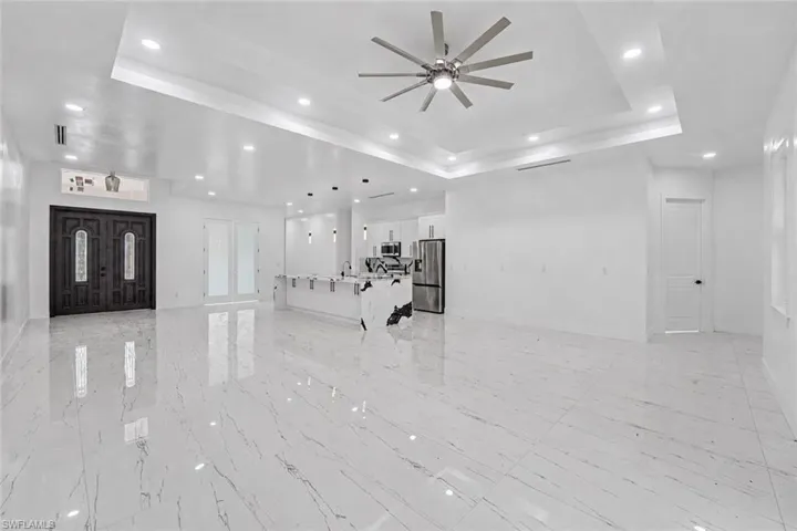 Expansive open-concept interior featuring large format marble-look tile flooring, a tray ceiling with recessed lighting, and a modern ceiling fan