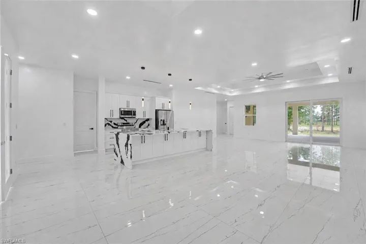 Open-concept living area featuring large format porcelain tile flooring, a kitchen island with a waterfall countertop, recessed lighting, and a tray ceiling with a ceiling fan
