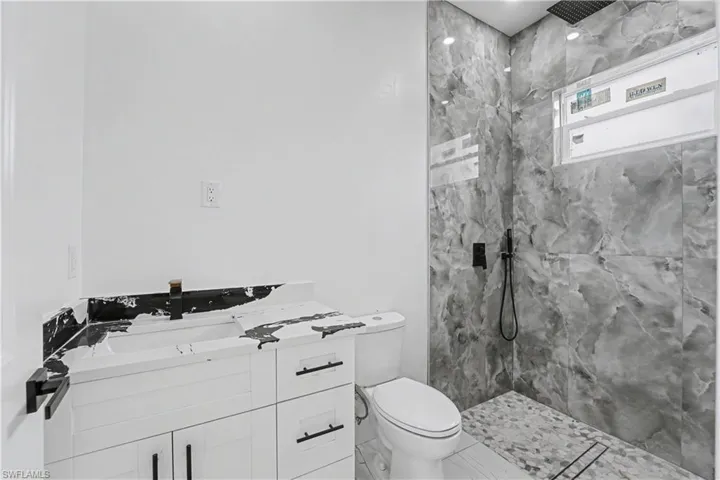 Bathroom featuring a white vanity with black hardware, a wall-mounted faucet, and a shower with large format marble-look tile walls