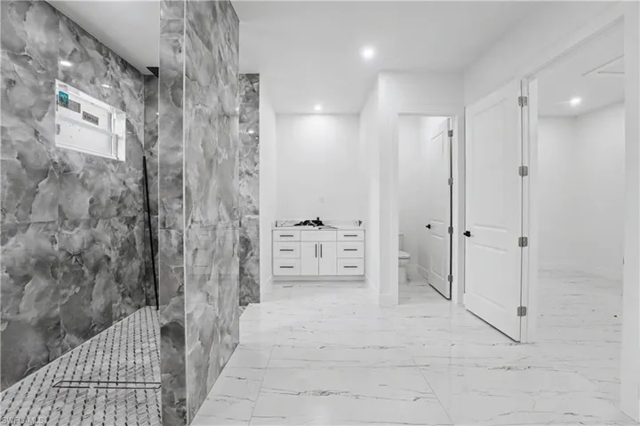 Spacious bathroom featuring large format marble-look floor tiling, a walk-in shower with stone-patterned wall tiles and mosaic floor tiling, and a white vanity with integrated cabinetry