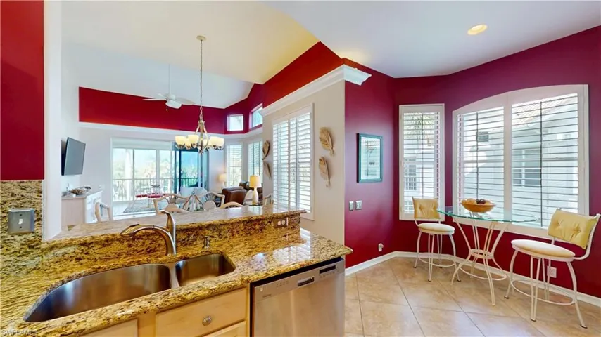 Kitchen with stainless steel dishwasher, light stone counters, light tile patterned floors, a peninsula, and a chandelier