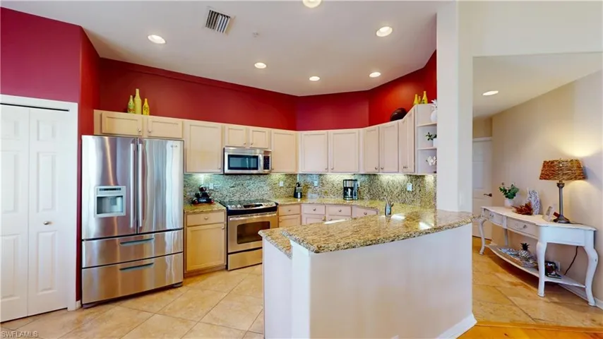 Kitchen with appliances with stainless steel finishes, decorative backsplash, open shelves, light stone countertops, and a peninsula