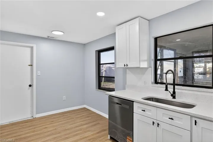 Kitchen featuring white cabinetry, stainless steel dishwasher, light wood-type flooring, light stone countertops, and decorative backsplash
