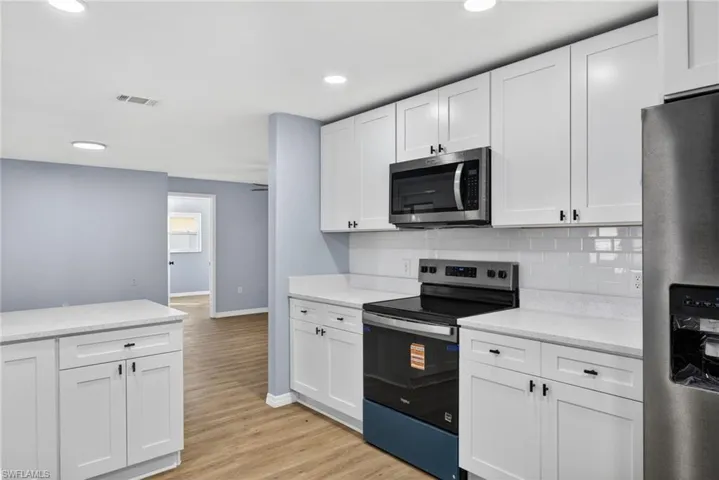 Kitchen with stainless steel appliances, white cabinetry, light wood-style floors, tasteful backsplash, and recessed lighting