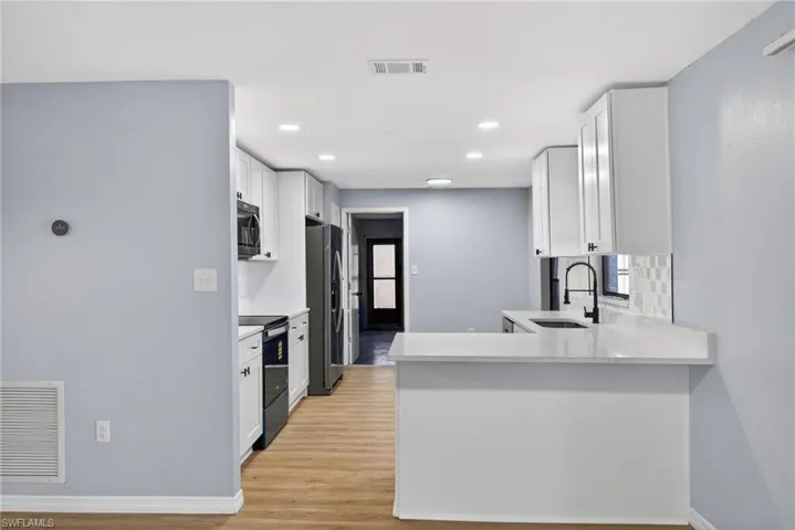 Kitchen featuring white cabinetry, a peninsula, electric range, light stone counters, and stainless steel fridge