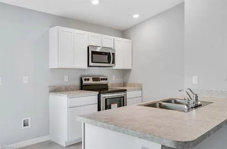 Kitchen with stainless steel appliances, white cabinetry, a peninsula, light countertops, and recessed lighting
