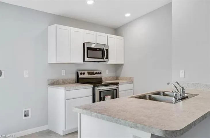 Kitchen with appliances with stainless steel finishes, a peninsula, white cabinetry, light countertops, and recessed lighting