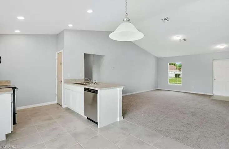 Kitchen featuring a peninsula, light colored carpet, white cabinetry, lofted ceiling, and decorative light fixtures