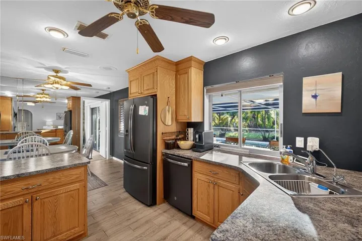 Kitchen with refrigerator with ice dispenser, dishwasher, dark countertops, light wood-style flooring, and ceiling fan