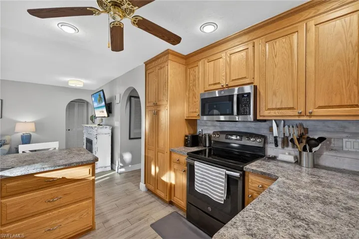 Kitchen with black range with electric cooktop, arched walkways, a ceiling fan, light wood-type flooring, and stainless steel microwave