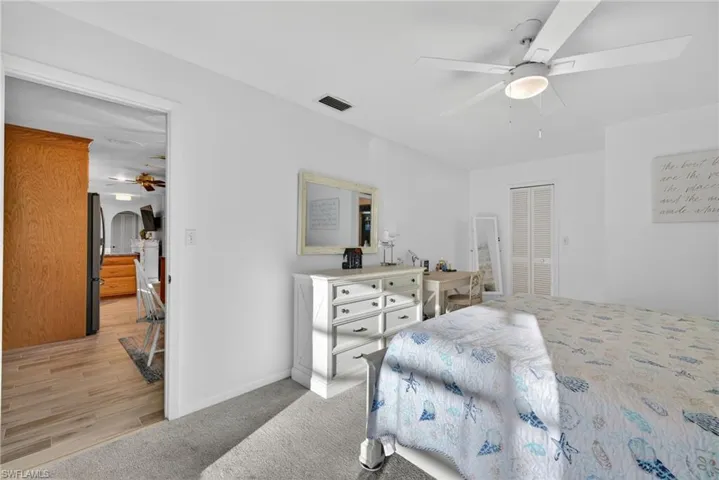 Bedroom with ceiling fan, a closet, arched walkways, freestanding refrigerator, and light carpet