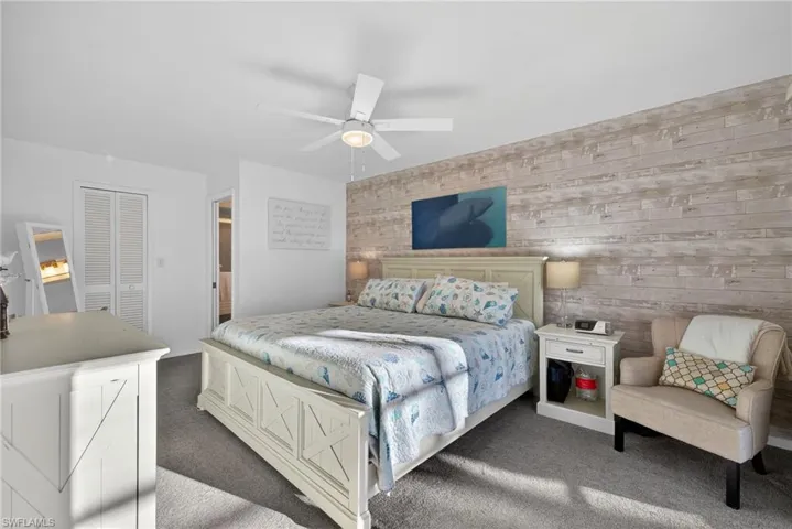 Carpeted bedroom with wood walls, a closet, an accent wall, and a ceiling fan