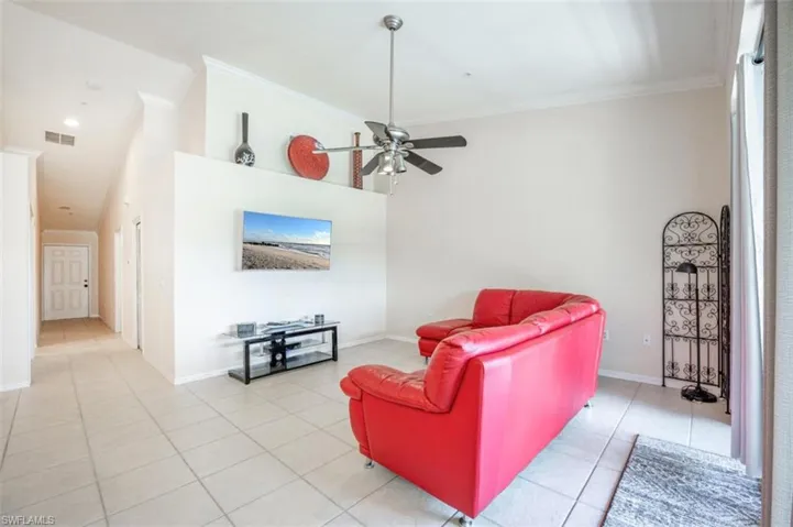 Living room featuring a high ceiling, crown molding, ceiling fan, and light tile patterned floors