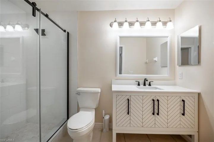 Bathroom with vanity, a shower with shower door, toilet, and tile patterned flooring