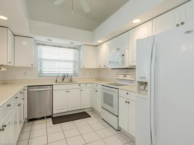 Kitchen featuring white cabinetry, sink, light tile patterned floors, and white appliances