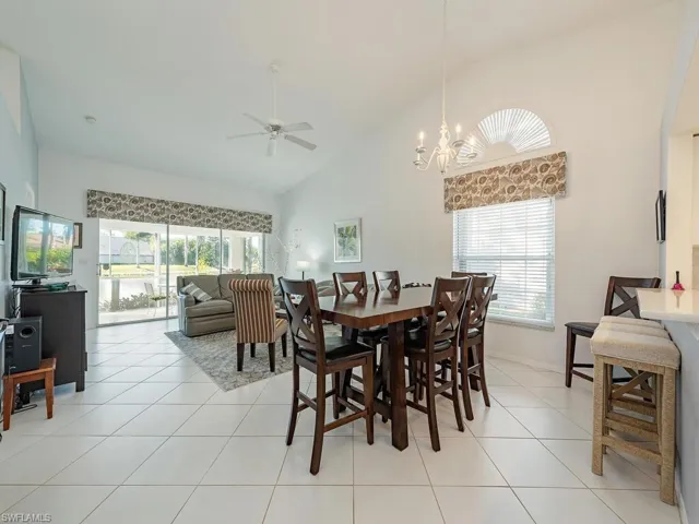 Tiled dining room featuring plenty of natural light, ceiling fan with notable chandelier, and high vaulted ceiling