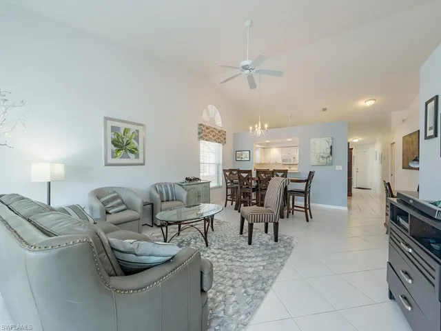 Living room featuring light tile patterned floors, ceiling fan with notable chandelier, and high vaulted ceiling