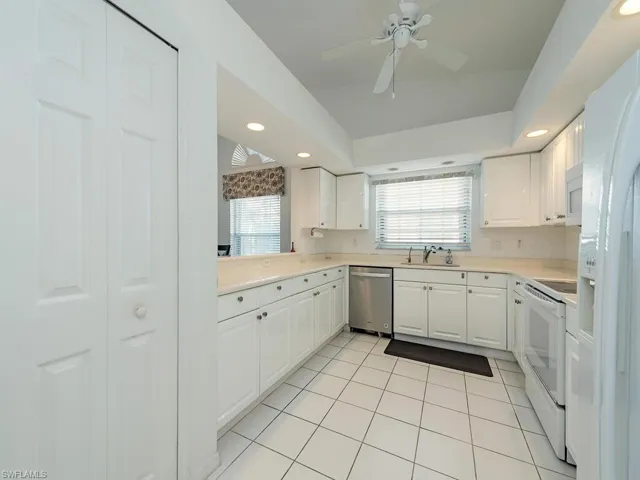 Kitchen with tasteful backsplash, white appliances, sink, light tile patterned floors, and white cabinets