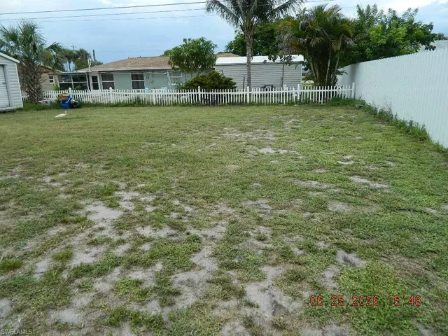 Expansive grassy yard area featuring a picket fence, privacy fence, and mature palm trees