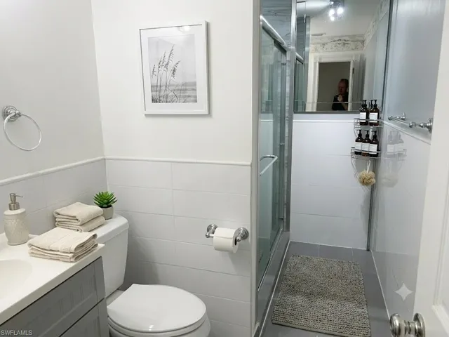 Virtually Staged Bathroom featuring a shower stall with clear glass enclosure and chrome hardware, white tile walls, light gray floor tiles, and a white vanity with a gray cabinet base