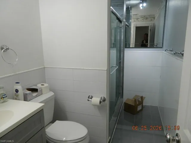 Bathroom featuring a glass-enclosed shower, white tiled walls, a vanity with a white countertop, and a toilet