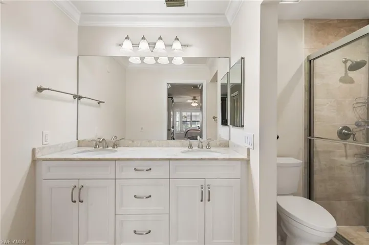 Bathroom featuring a stall shower, crown molding, double vanity, and ensuite bath