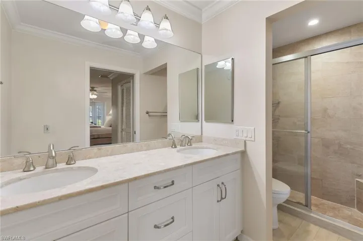 Ensuite bathroom featuring crown molding, a stall shower, double vanity, and a ceiling fan