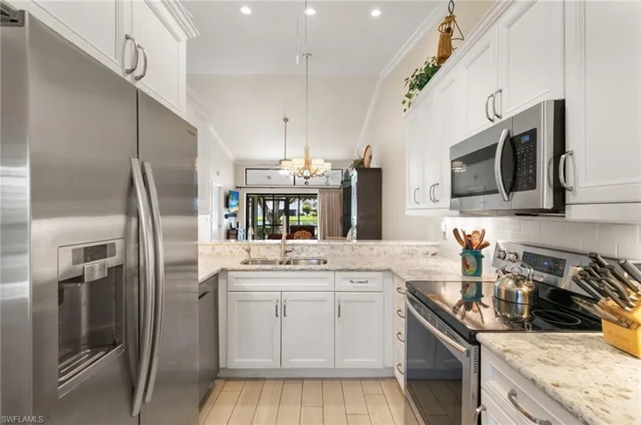 Kitchen with stainless steel appliances, white cabinets, ornamental molding, light stone countertops, and hanging light fixtures