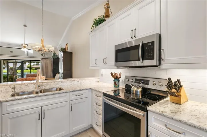 Kitchen featuring stainless steel appliances, white cabinetry, crown molding, light stone counters, and vaulted ceiling