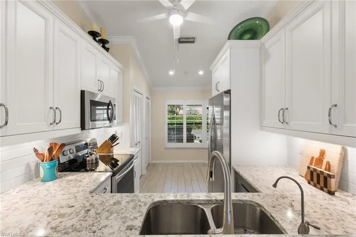 Kitchen featuring backsplash, appliances with stainless steel finishes, light stone countertops, white cabinetry, and ornamental molding