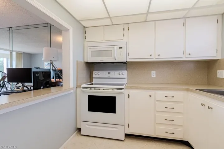 Kitchen featuring white cabinetry, a drop ceiling, tasteful backsplash, white appliances, and light tile patterned floors