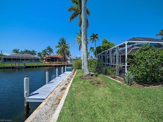 View of dock with glass enclosure, a lawn, and a water view
