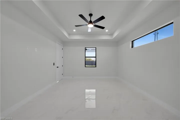 Unfurnished room featuring light marble finish floors, recessed lighting, a tray ceiling, and ceiling fan