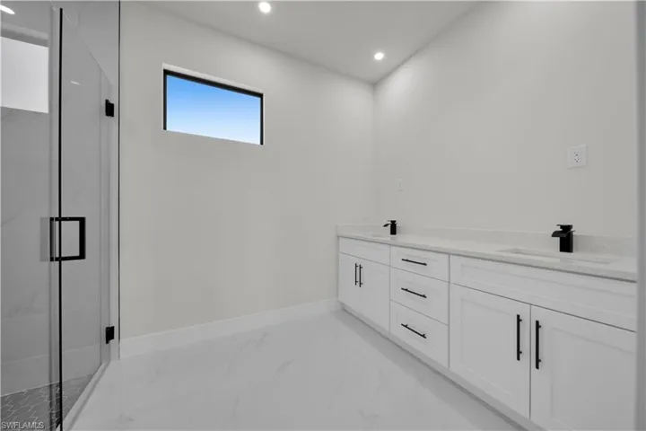 Full bath featuring double vanity, recessed lighting, a marble finish shower, and light marble finish flooring