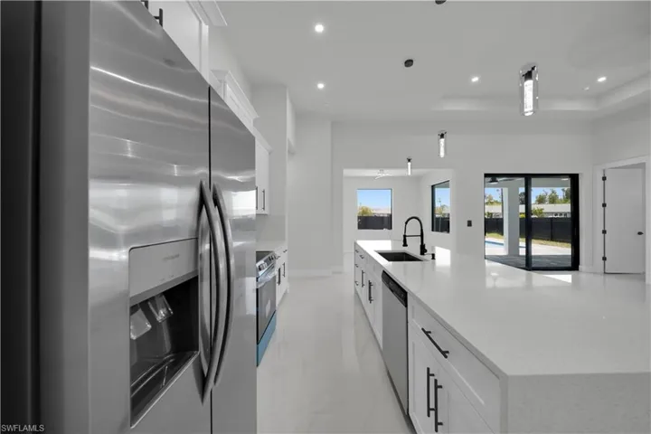 Kitchen with stainless steel appliances, white cabinetry, light stone countertops, a large island, and a tray ceiling