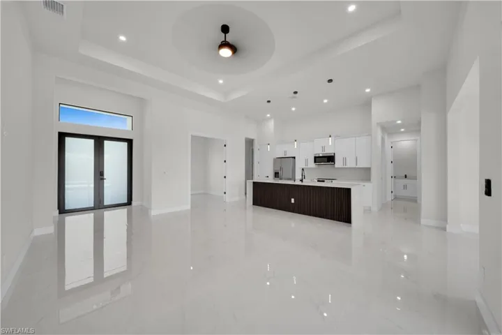 Kitchen with open floor plan, white cabinets, a large island with sink, a high tray ceiling, and a ceiling fan