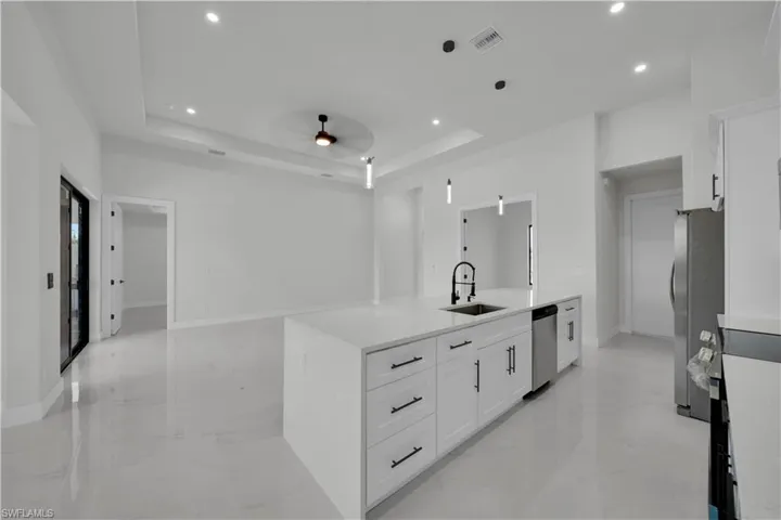 Kitchen with white cabinets, hanging light fixtures, light stone counters, stainless steel appliances, and ceiling fan