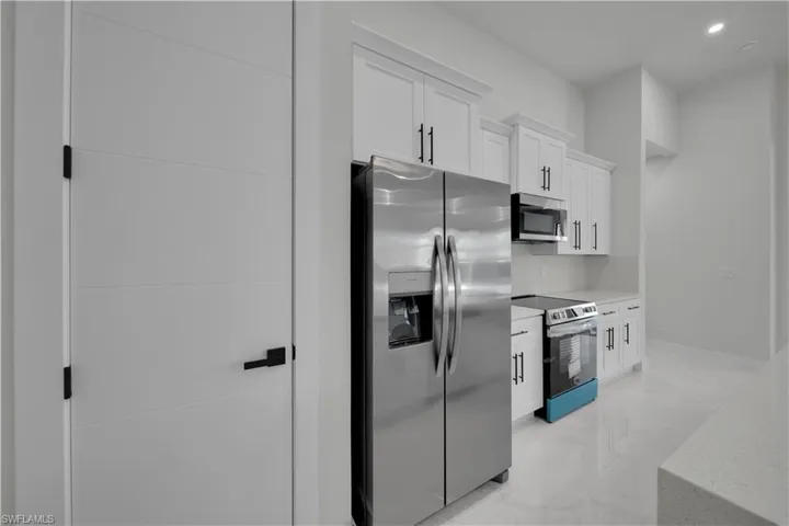 Kitchen featuring stainless steel appliances, white cabinets, recessed lighting, light marble finish floors, and light stone counters