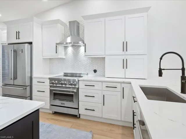 Kitchen featuring sink, wall chimney exhaust hood, light hardwood / wood-style floors, white cabinets, and appliances with stainless steel finishes