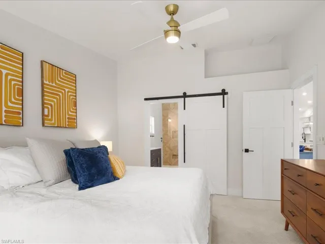 Carpeted bedroom featuring a barn door, ceiling fan, and connected bathroom