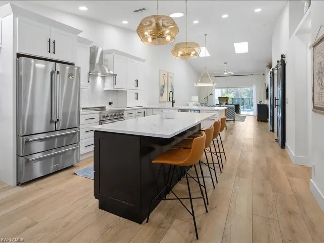 Kitchen featuring wall chimney range hood, a barn door, kitchen peninsula, decorative light fixtures, and appliances with stainless steel finishes