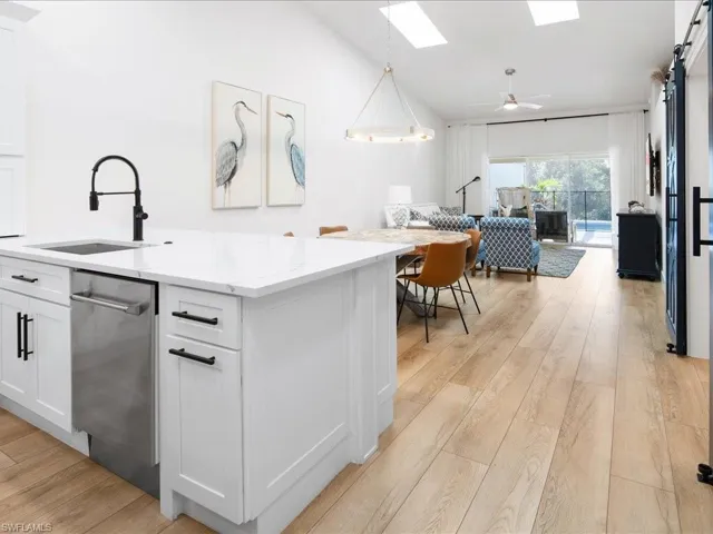 Kitchen with sink, white cabinetry, hanging light fixtures, and light hardwood / wood-style flooring