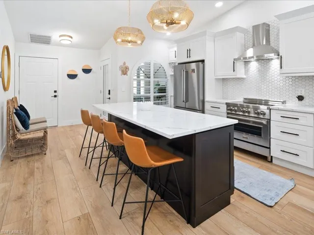 Kitchen featuring white cabinets, high end appliances, wall chimney range hood, a chandelier, and a center island