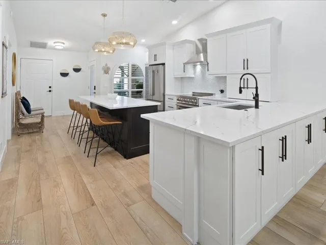 Kitchen featuring white cabinets, hanging light fixtures, wall chimney exhaust hood, premium appliances, and a kitchen island