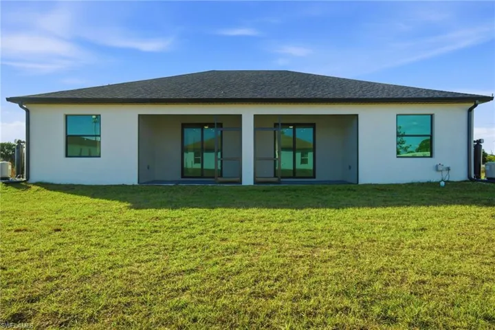 Rear view of property with stucco siding, a patio area, a lawn, and roof with shingles