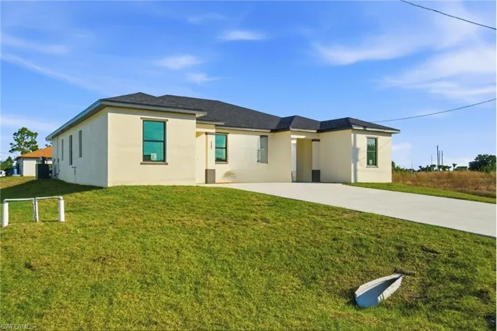 Rear view of property featuring a lawn, concrete driveway, and stucco siding