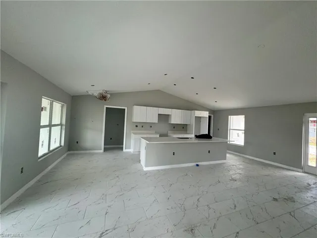 Unfurnished living room featuring lofted ceiling, baseboards, and light marble finish floors