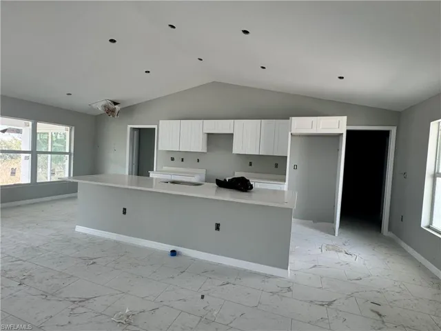 Kitchen featuring light marble finish floors, vaulted ceiling, white cabinetry, a center island, and baseboards