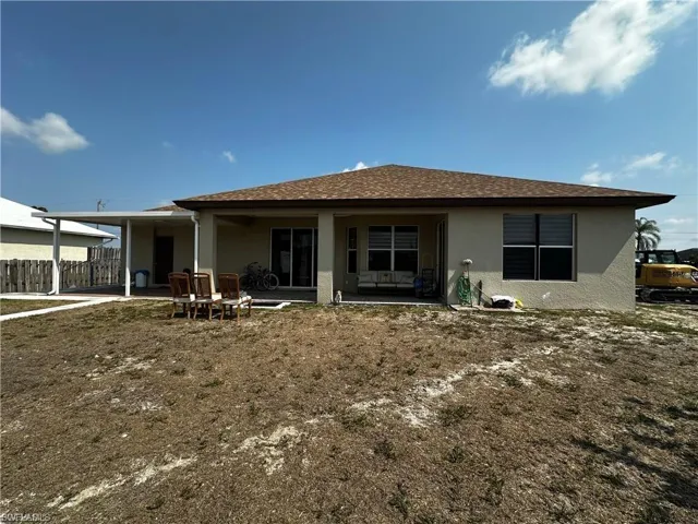 Rear view of house with stucco siding, a patio, and roof with shingles